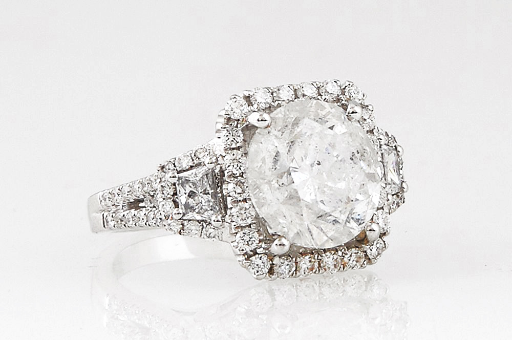 Lady's 18K White Gold Dinner Ring, with a 5.03 ct. round diamond atop a border of small round diamonds, flanked by baguette diamond lugs within diamond
